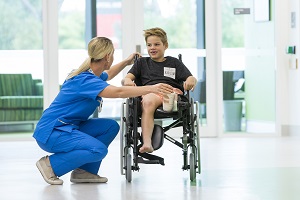 A nurse crouches beside a young boy in a wheelchair