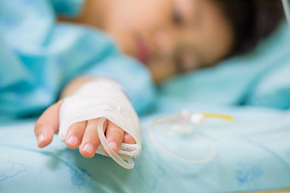 Child with cannula in wrist, lying in bed